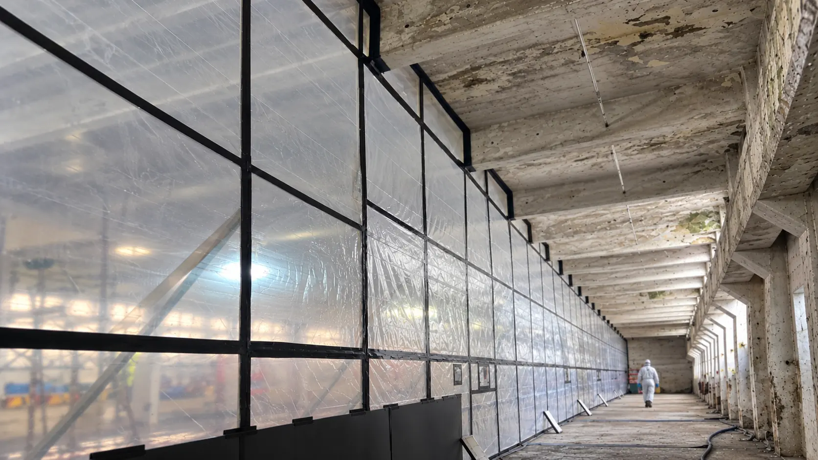 Composite image based on a real asbestos containment enclosure photograph, with a protected worker walking away